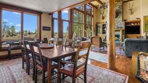 A spacious dining area with a large wooden table and chairs, a fireplace, and a view of the outdoors. - RMR: Mallory House in The Aspens/Wilson,WY (Wilson)