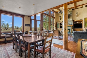 A spacious dining area with a large wooden table and chairs, a fireplace, and a view of the outdoors.