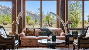 A room with large windows, a sofa, two armchairs, a coffee table, and a lamp. - RMR: Mallory House in The Aspens/Wilson,WY (Wilson)