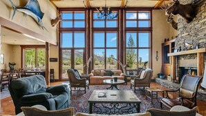 A spacious living room with large windows, a fireplace, and mounted animal heads. - RMR: Mallory House in The Aspens/Wilson,WY (Wilson)