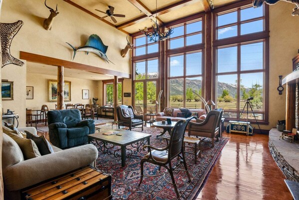 A spacious living room with large windows, a ceiling fan, and various mounted animal heads.