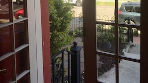 Blick durch ein großes Bogenfenster mit Backsteinfassade auf eine Straße mit parkenden Autos und einer grünen Rasenfläche.
