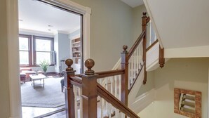 Eine Treppe mit Holzspindeln und einer weißen Brüstung, die zu einem gut beleuchteten Raum mit Bücherregal und Essbereich führt.