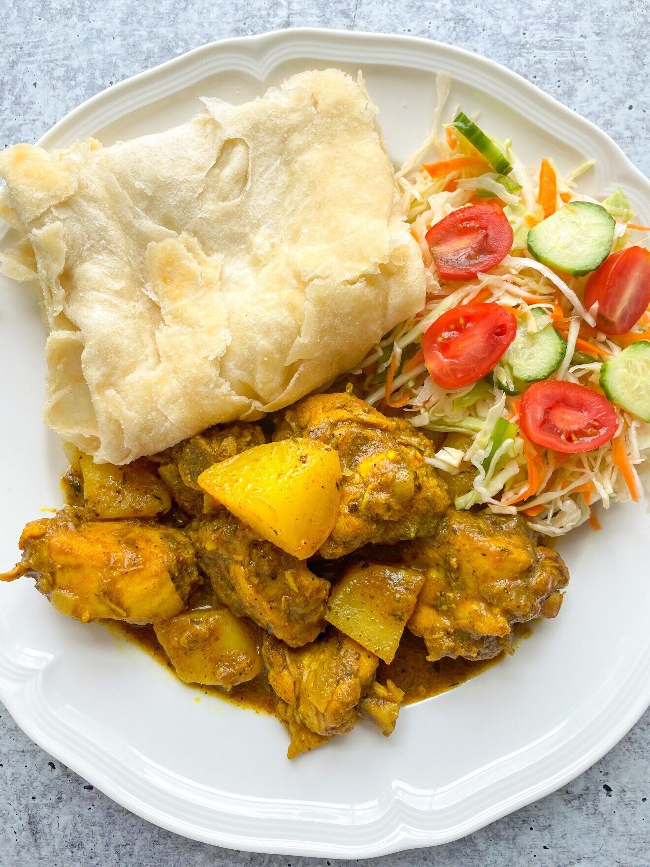 Une assiette contenant un plat de curry, du pain plat et une salade de légumes.