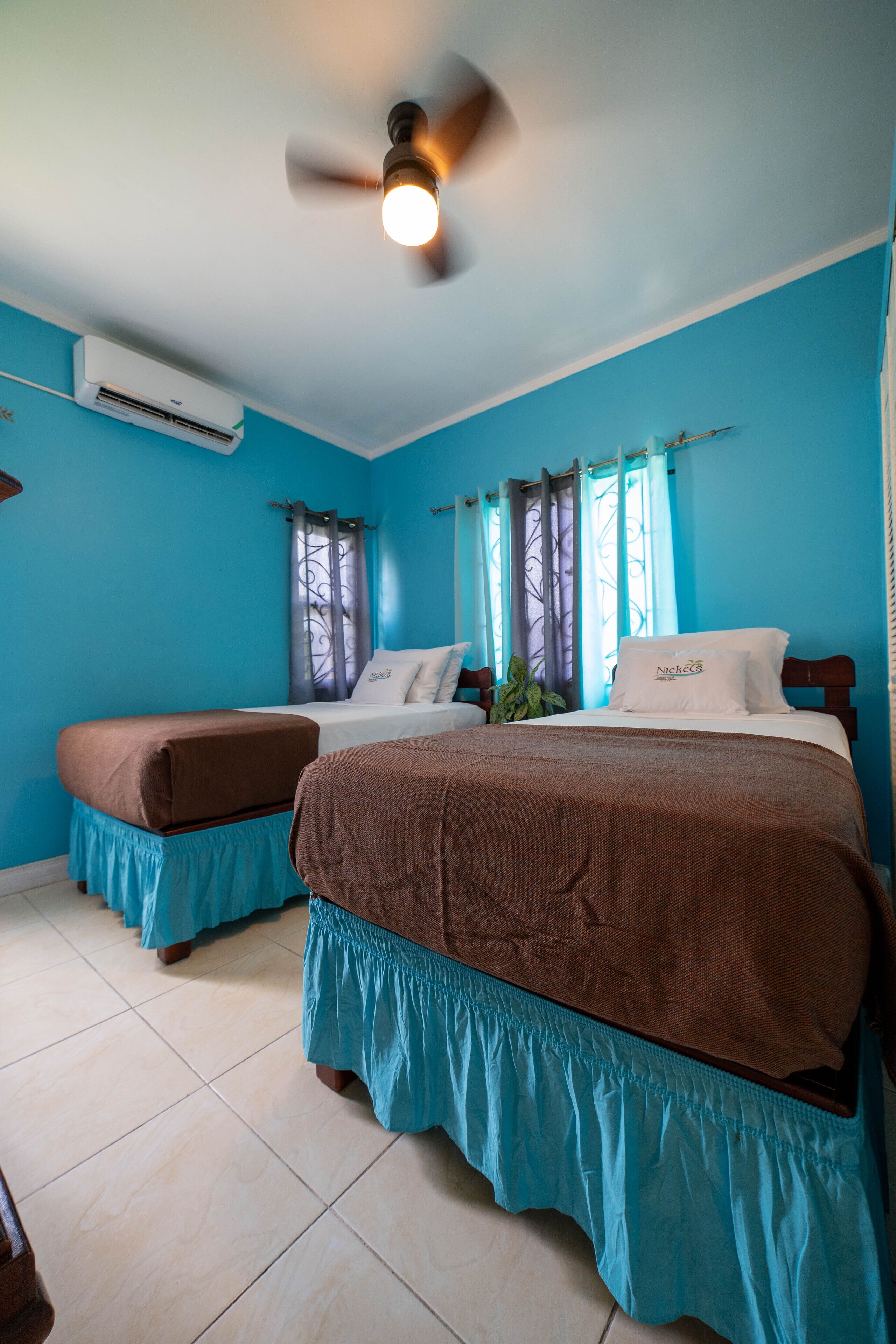 A hotel room with two beds, a ceiling fan, and an air conditioning unit.