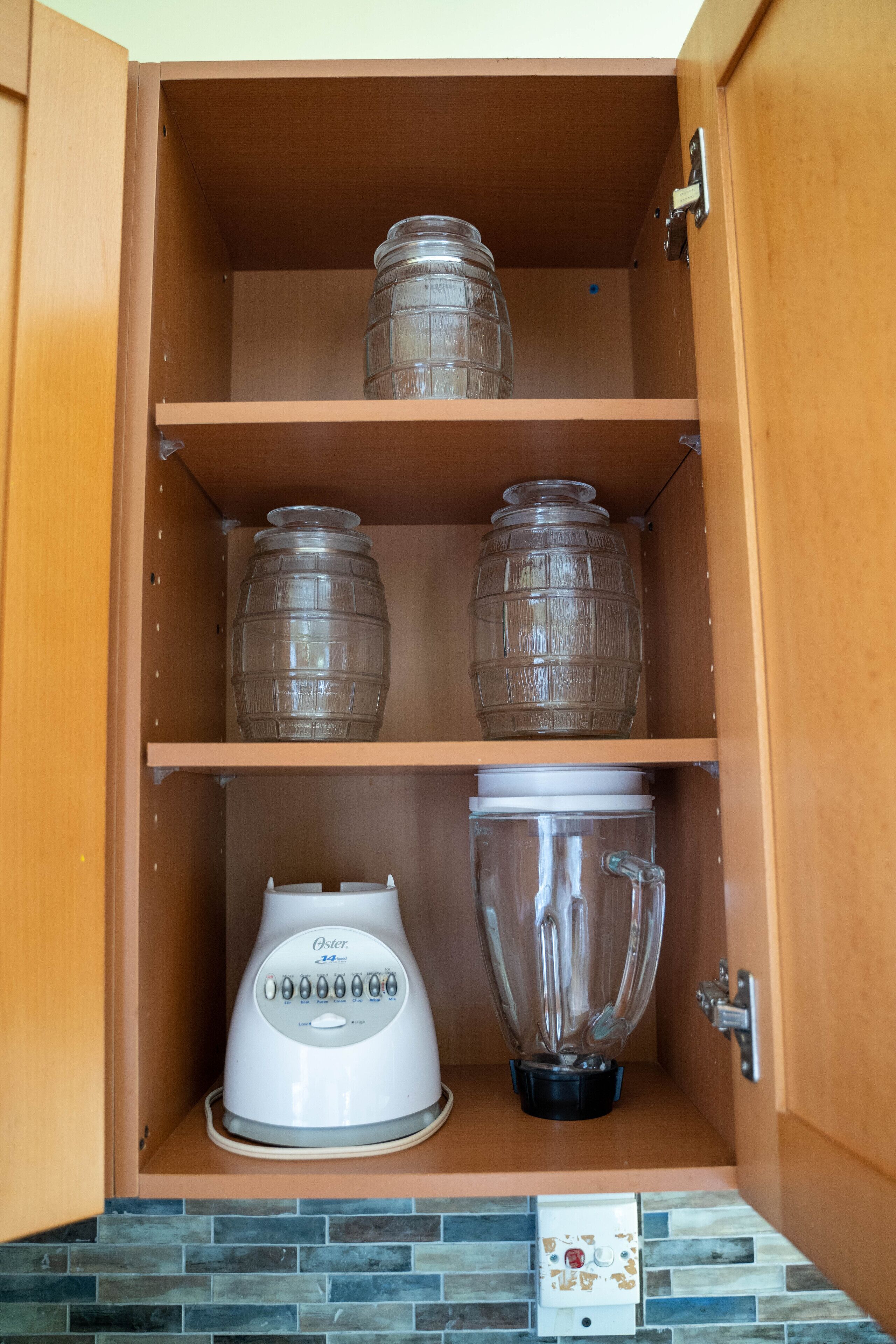 A kitchen cabinet with a blender, two glass containers, and a water dispenser.