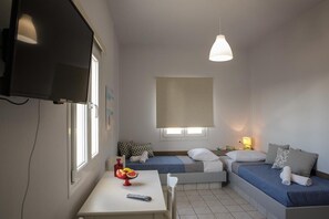 A small, well-lit room with a TV, a table with a fruit bowl, two beds, and a window. - Irene Beach (Hersonissos)