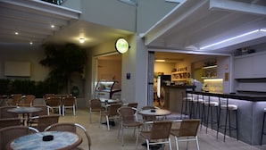 An outdoor cafe area with wicker chairs and tables, a bar with stools, and a neon sign for 'Mythos'. - Blue Horizon Apartments (Mylopotamos)