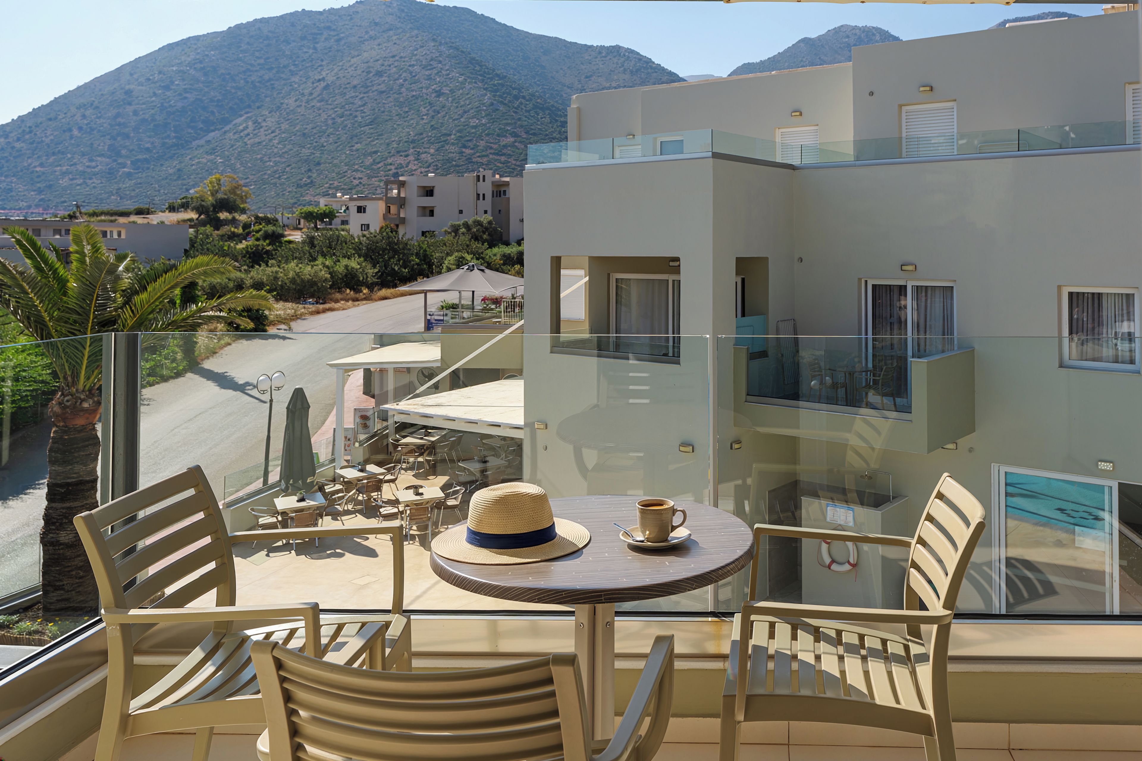 A balcony with a table and chairs, overlooking a street and buildings with mountains in the background.