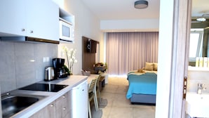 A modern hotel room with a kitchenette, a bed with a blue bedspread, and a bathroom with a sink and mirror. - Blue Horizon Apartments (Mylopotamos)