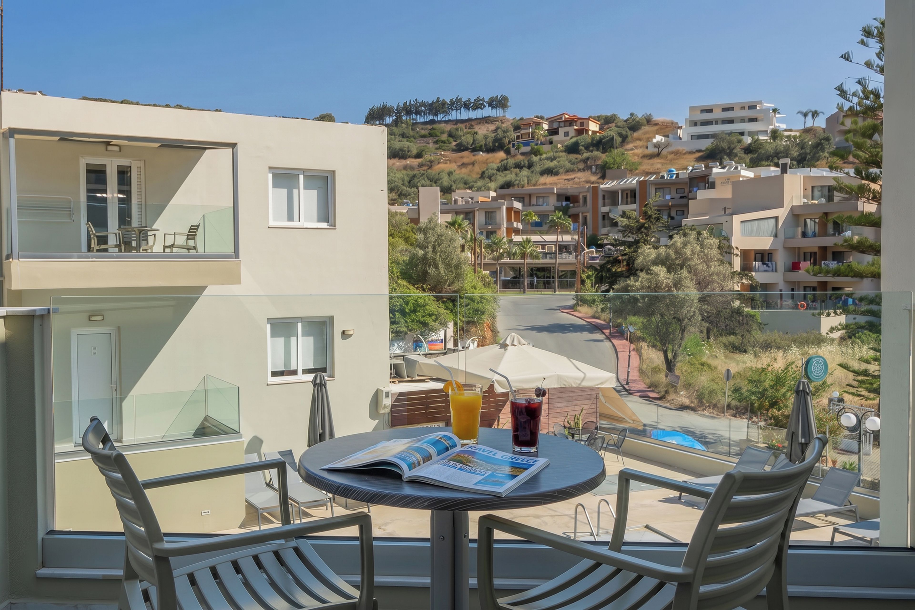 A balcony with a table, chairs, and a magazine, overlooking a residential area with houses and a hill.