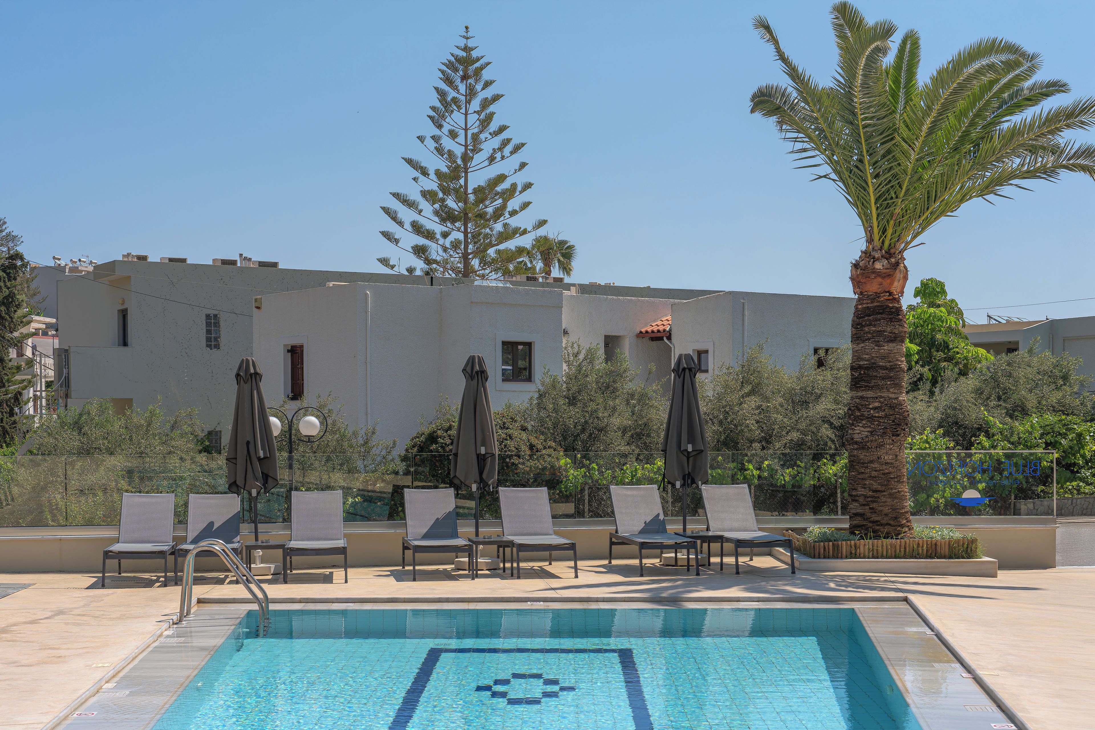 A swimming pool with lounge chairs and umbrellas, surrounded by trees and a building.