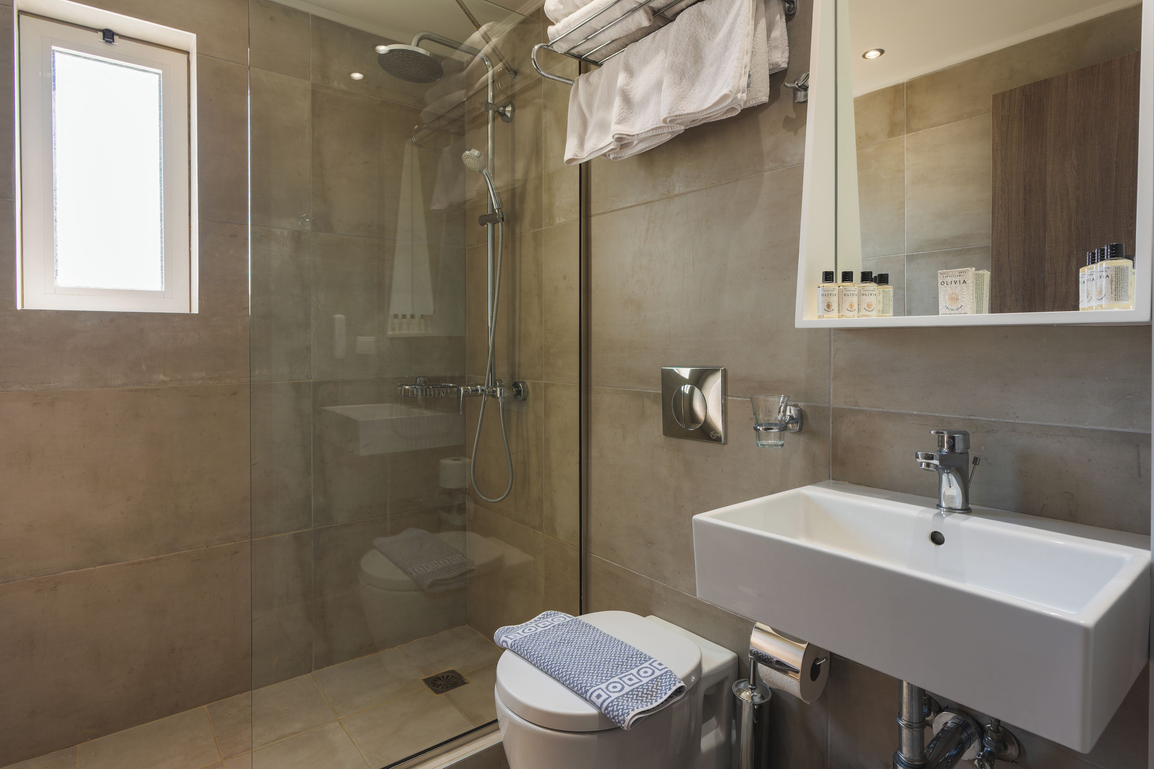 Un baño moderno con ducha envuelta en vidrio, un lavamanos blanco y un inodoro con una toalla.