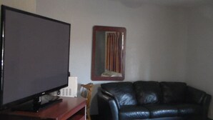 A living room with a flat-screen TV on a stand, a wooden chair, and a black leather sofa. - Laurel Inn (Oakland)