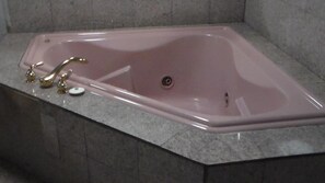 A rectangular bathtub with a single faucet and a drain, set in a corner with a tiled floor. - Laurel Inn (Oakland)