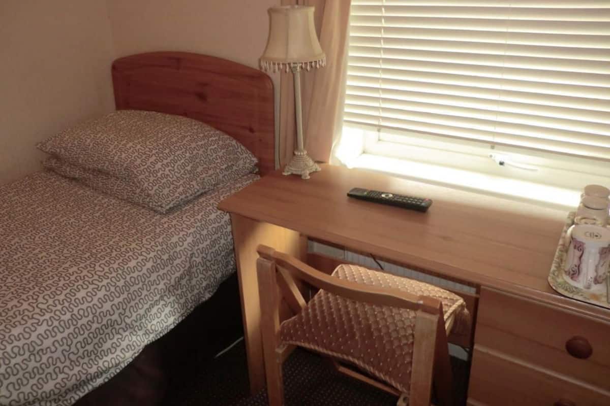 Un dormitorio con cama de madera, un escritorio con lámpara, una silla y una ventana con persianas.