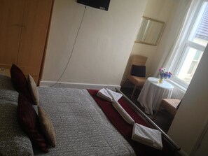 Une chambre d’hôtel avec un lit, une petite table sur laquelle est posé un vase de fleurs, une chaise et une fenêtre donnant sur un paysage agréable.