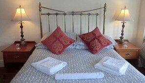 Un lit bien fait, agrémenté de deux oreillers rouges, de deux serviettes blanches et de deux lampes de chevet posées sur des tables de nuit en bois.