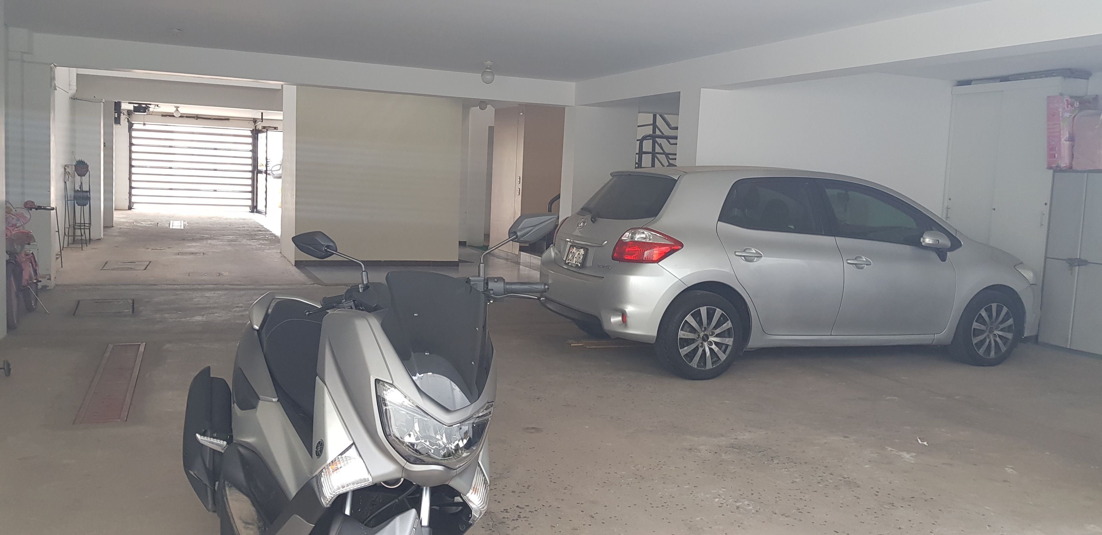 Un garage dans lequel se trouvent une voiture argentée et un scooter.