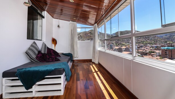 Un balcón con piso de madera y una cama con manta verde.