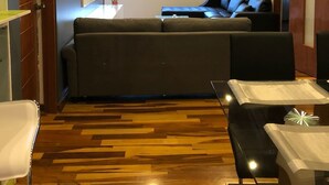 Una sala de estar moderna con un sofá de color oscuro, una mesa de centro de vidrio y piso de madera.