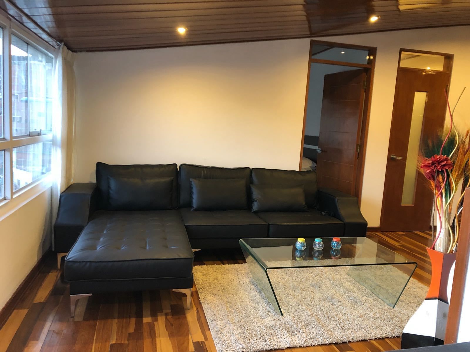 Ein modernes Wohnzimmer mit einer Eckcouch, einem Glastisch und Holzboden.