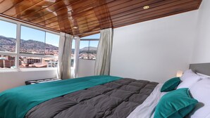 Un dormitorio con una cama grande, vistas de un paisaje urbano a través de una ventana y techo de madera.