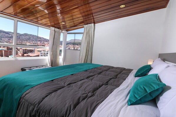 Un dormitorio con una cama grande, vistas de un paisaje urbano a través de una ventana y techo de madera.