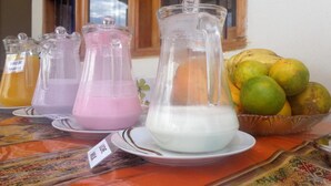 A table with three pitchers of different colored beverages and a bowl of fruits. - Pampa & Selva Hotel (Rurrenabaque)