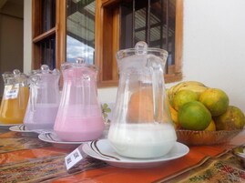 Una mesa con tres jarras de bebidas de colores diferentes y un bol de frutas.