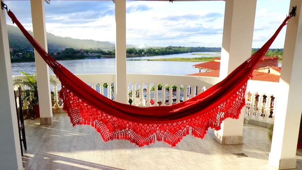 A hammock hanging between white columns with a view of a river and mountains. - Pampa & Selva Hotel (Rurrenabaque)