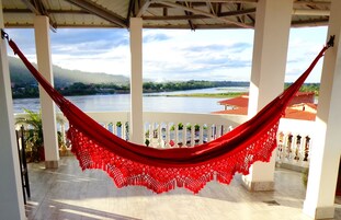 Una hamaca suspendida entre columnas blancas, con vistas a un río y montañas.