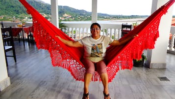 Une personne est assise dans un hamac rouge sur une terrasse, d’où l’on a une vue sur un lac et des collines.