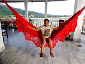 A person sitting in a red hammock on a terrace with a view of a lake and hills. - Pampa & Selva Hotel (Rurrenabaque)