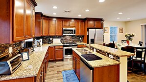 Una cocina moderna con armarios de madera, encimeras de granito y electrodomésticos de acero inoxidable, además de un comedor con mesa y sillas.