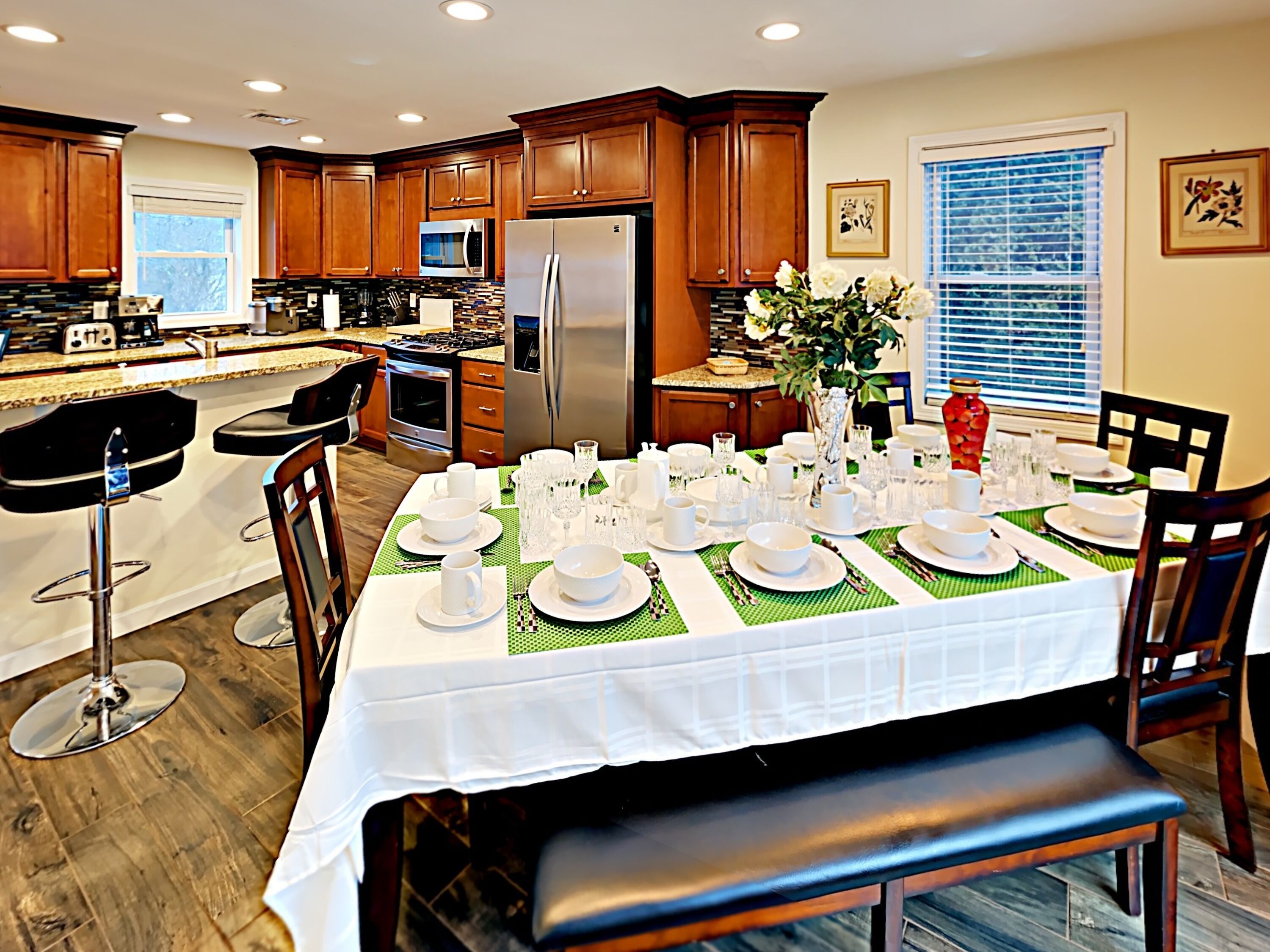 A modern kitchen with wooden cabinets, stainless steel appliances, and a dining area set for a meal.