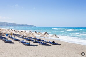 A beach with rows of blue lounge chairs and thatched umbrellas.
