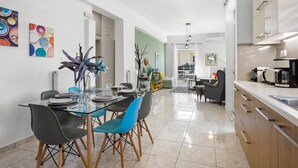 Una cocina moderna con una encimera y armarios, un comedor con una mesa de vidrio y sillas, y una sala de estar con un sofá y una mesa auxiliar.