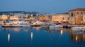 Un puerto deportivo con barcos amarrados, edificios frente al agua y un paisaje urbano al fondo.