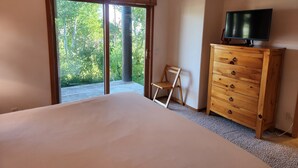 A bedroom with a large bed, a wooden dresser, a television on top, and a sliding glass door leading to a balcony.