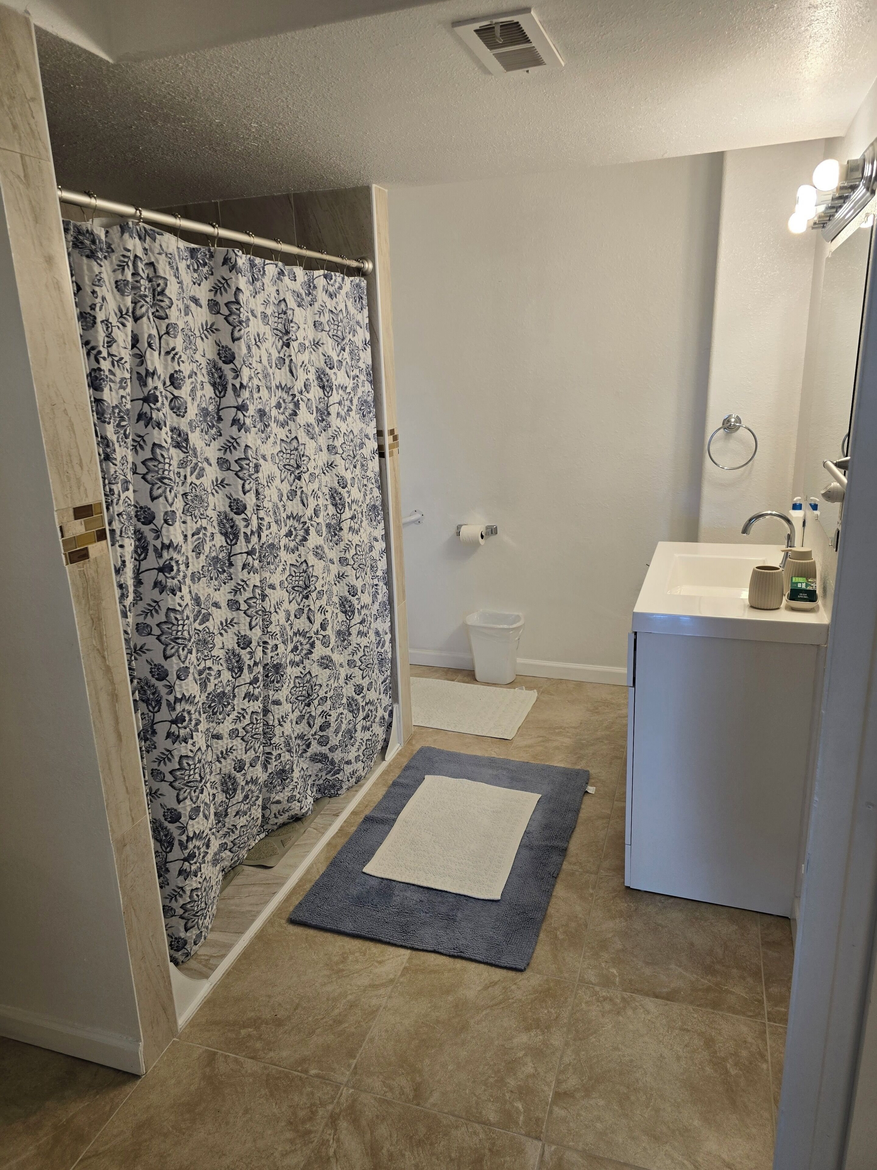 Un bagno con tenda doccia, un water, un lavandino con specchio e un tappeto sul pavimento.