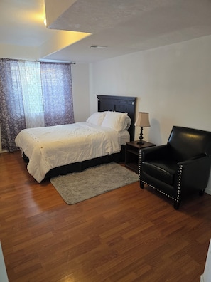 A bedroom with a bed, a chair, a nightstand, and a lamp.