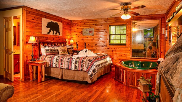 A log cabin-style bedroom with a wooden bed, a large window, a ceiling fan, and a green bathtub. - Gatlinburg Cabin, Tickets, Heart Whirlpool, Hot Tub Pool Table King Bed Internet (Gatlinburg)