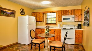 A compact kitchen with wooden cabinets, a white refrigerator, a microwave, and a stove. There is a small round table with chairs, and a decorative item on the table. - Gatlinburg Cabin, Tickets, Heart Whirlpool, Hot Tub Pool Table King Bed Internet (Gatlinburg)