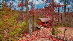 A cabin surrounded by trees with red leaves, a wooden deck, and a clear sky. - Gatlinburg Cabin, Tickets, Heart Whirlpool, Hot Tub Pool Table King Bed Internet (Gatlinburg)