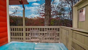 A hot tub with a wooden deck and chairs, surrounded by trees and a clear sky. - Gatlinburg Cabin, Tickets, Heart Whirlpool, Hot Tub Pool Table King Bed Internet (Gatlinburg)