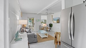 Et moderne køkken med et stort køleskab, et spiseområde med bord og stole, og en opholdsstue med sofa og lampe.