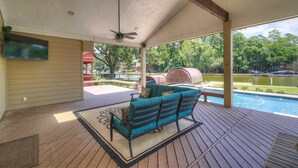 Un espacio al aire libre techado con piscina, un sofá azul y un ventilador de techo.