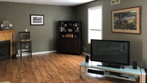 A living room with a fireplace, a television on a stand, a bookshelf, and a framed picture on the wall. - Magnificent & Spacious Condo for All of Your PSU Vacations 4.5 Miles from Campus (State College)