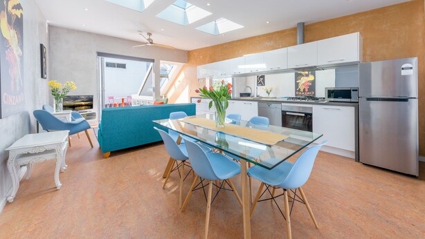 A modern kitchen with a glass dining table, blue chairs, and a stainless steel refrigerator. - Designer house in quiet street on city doorstep (Darlinghurst)